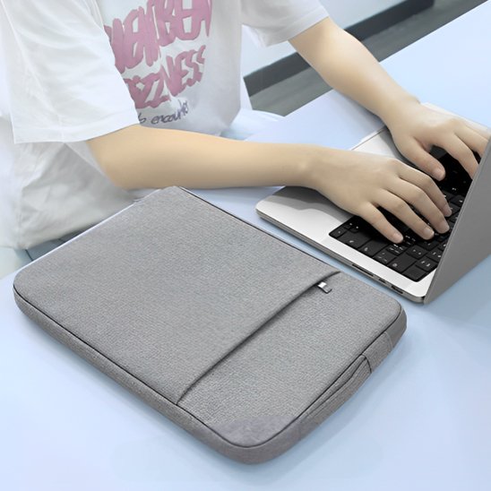 Housse PC portable grise imperméable posée près d'une personne qui travaille sur son ordinateur au bureau.